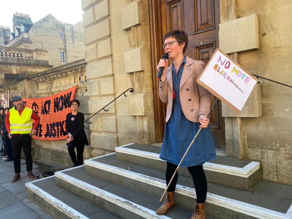 Saskia speaking at a climate protest in Bath holding a sign saying 'no more blah blah blah...'