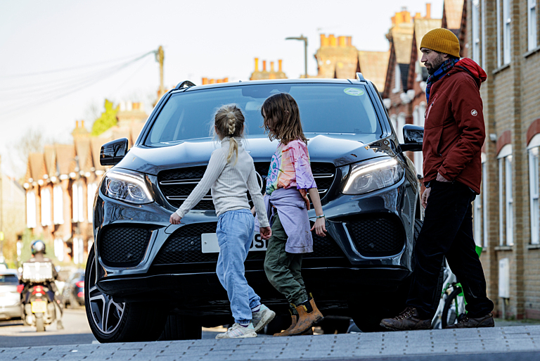 Credit: Crispin Hughes / Clean Cities Campaign / Climate Visuals

Two children and a parent walking in front of an SUV